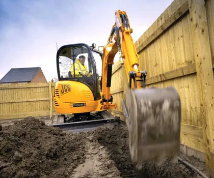 Mini digger excavating a trench beside a timber fence